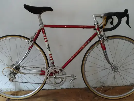 Rot lackiertes klassisches Rennrad mit Chromgabel vor heller Wand.